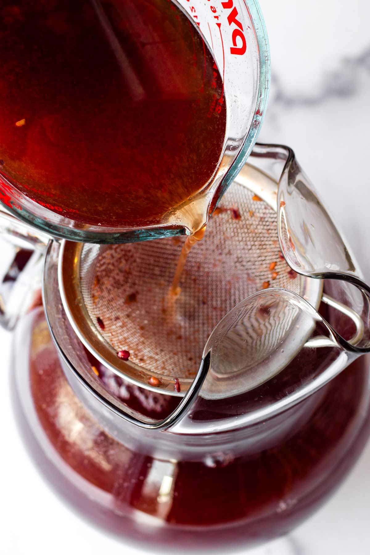 filtering blackberry iced tea through a sieve into a pitcher
