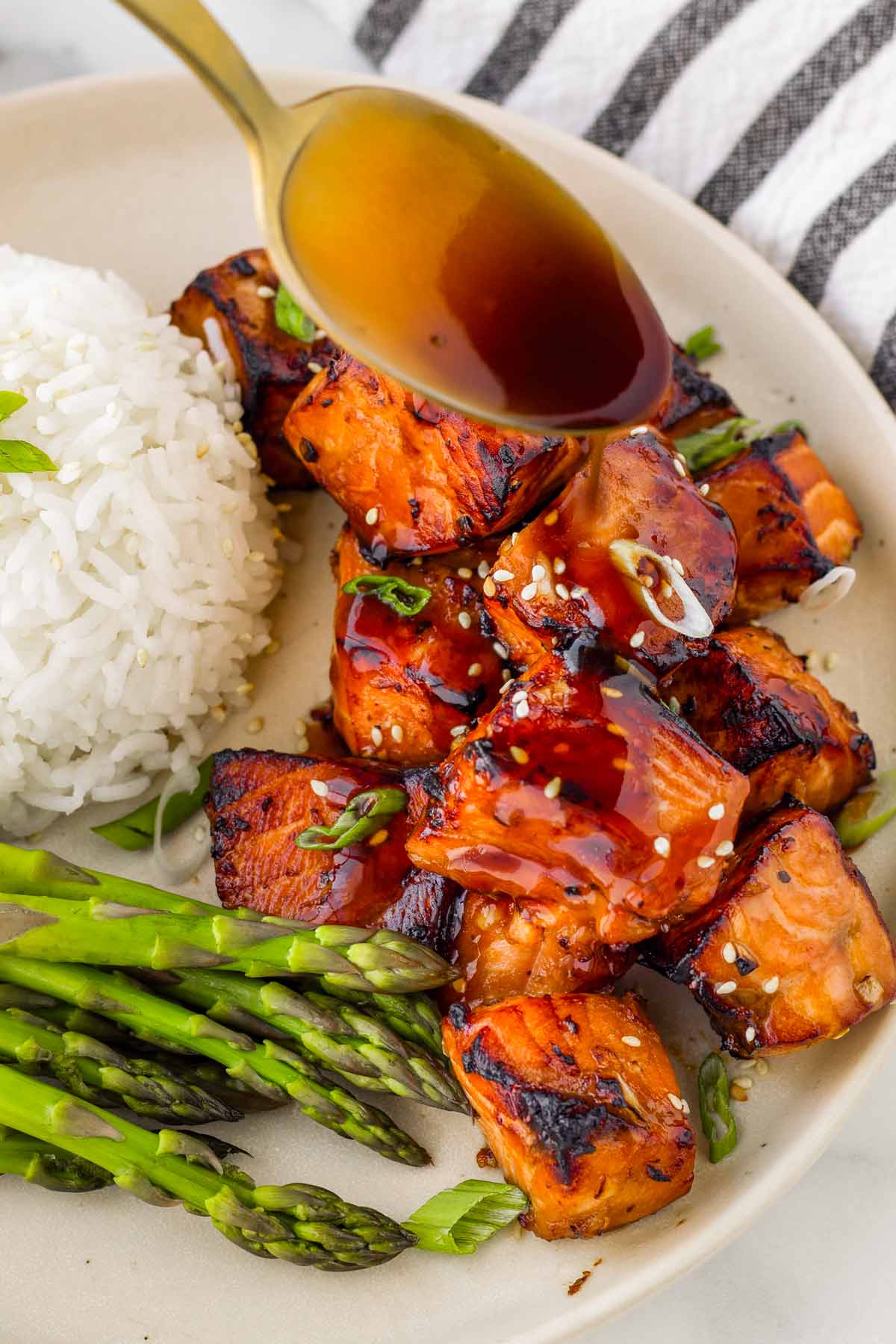 drizzling sauce over salmon bites on a plate with rice and asparagus