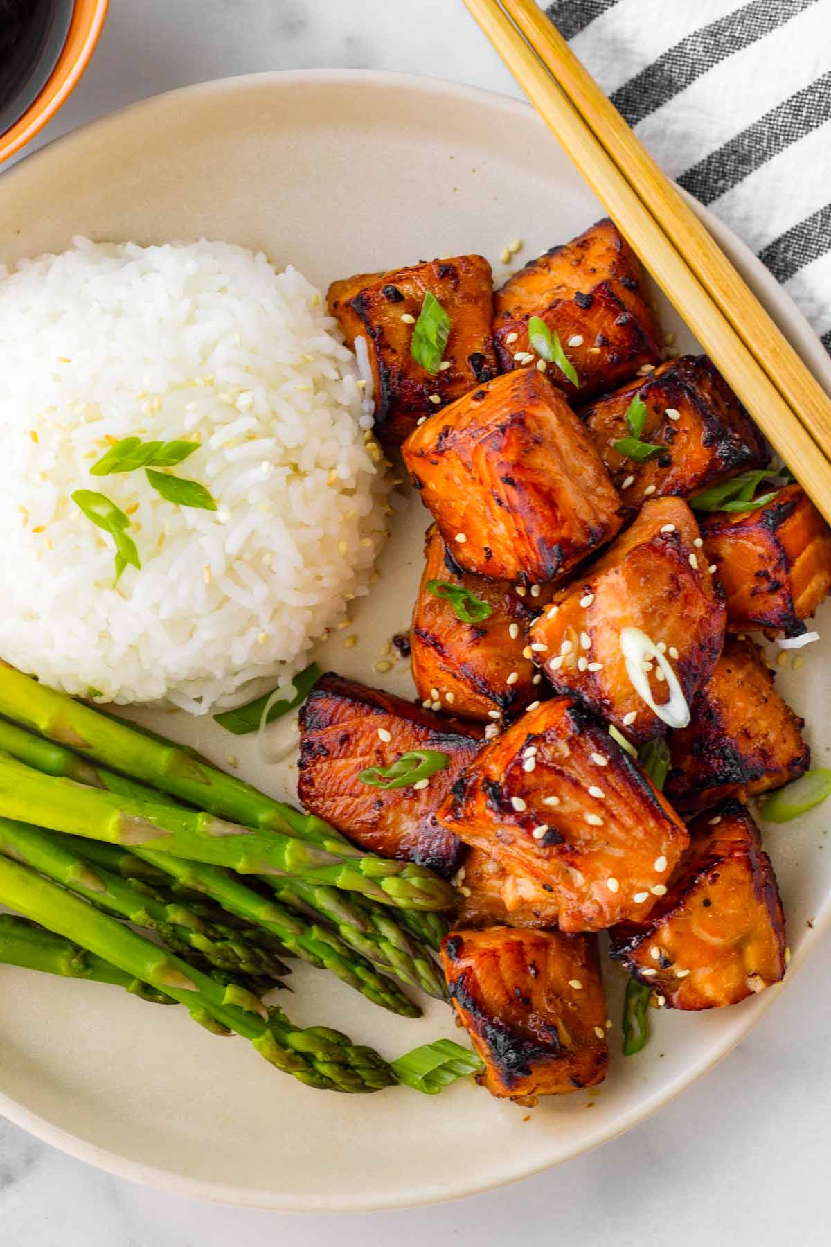 a plate with air fryer salmon bites with rice and asparagus and chopsticks