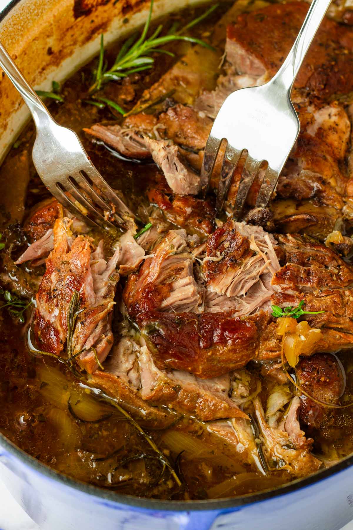 shredding braised pork roast in a dutch oven