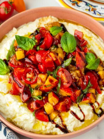 bowl of whipped burrata cheese with fruit and tomato topping