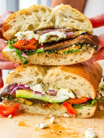 holding a stacked grilled vegetable sandwich on top of board