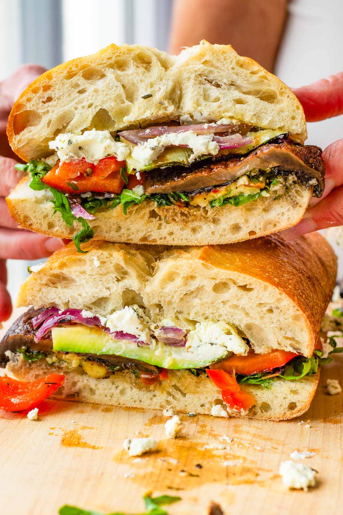 holding a stacked grilled vegetable sandwich on top of board