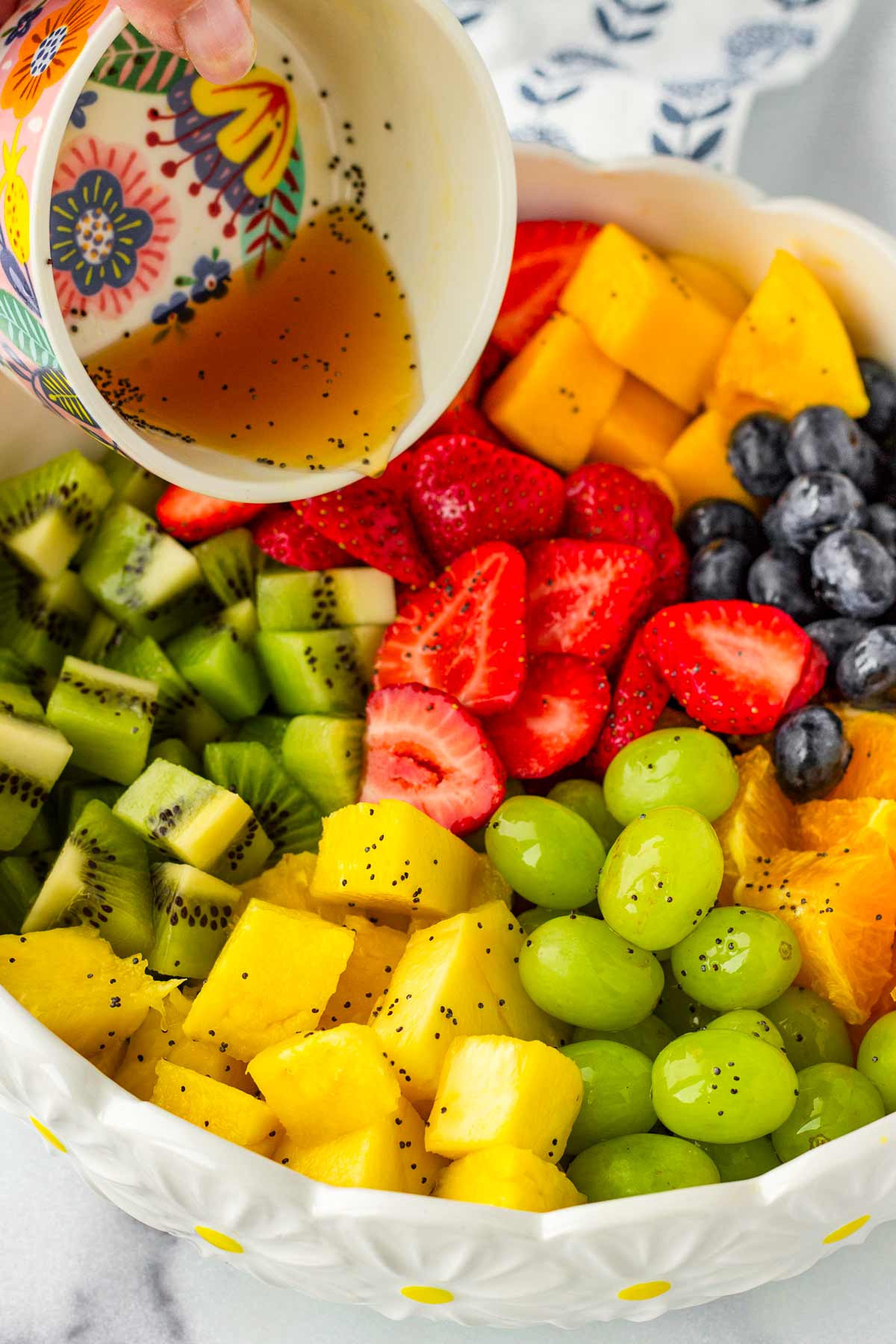 adding dressing to the chopped fruit in a bowl