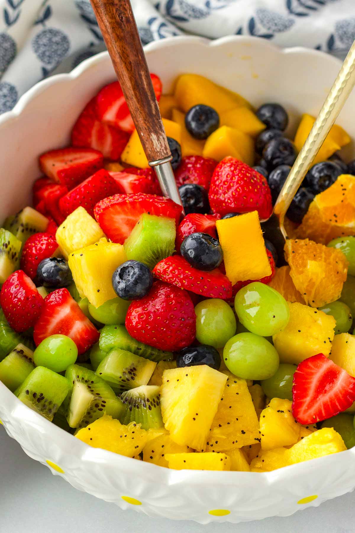 tossing diced fruit in a bowl with orange poppy seed dressing