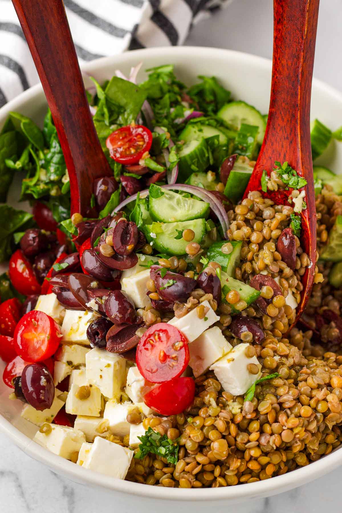tossing mediterranean lentil salad ingredients in a bowl with wooden spoons