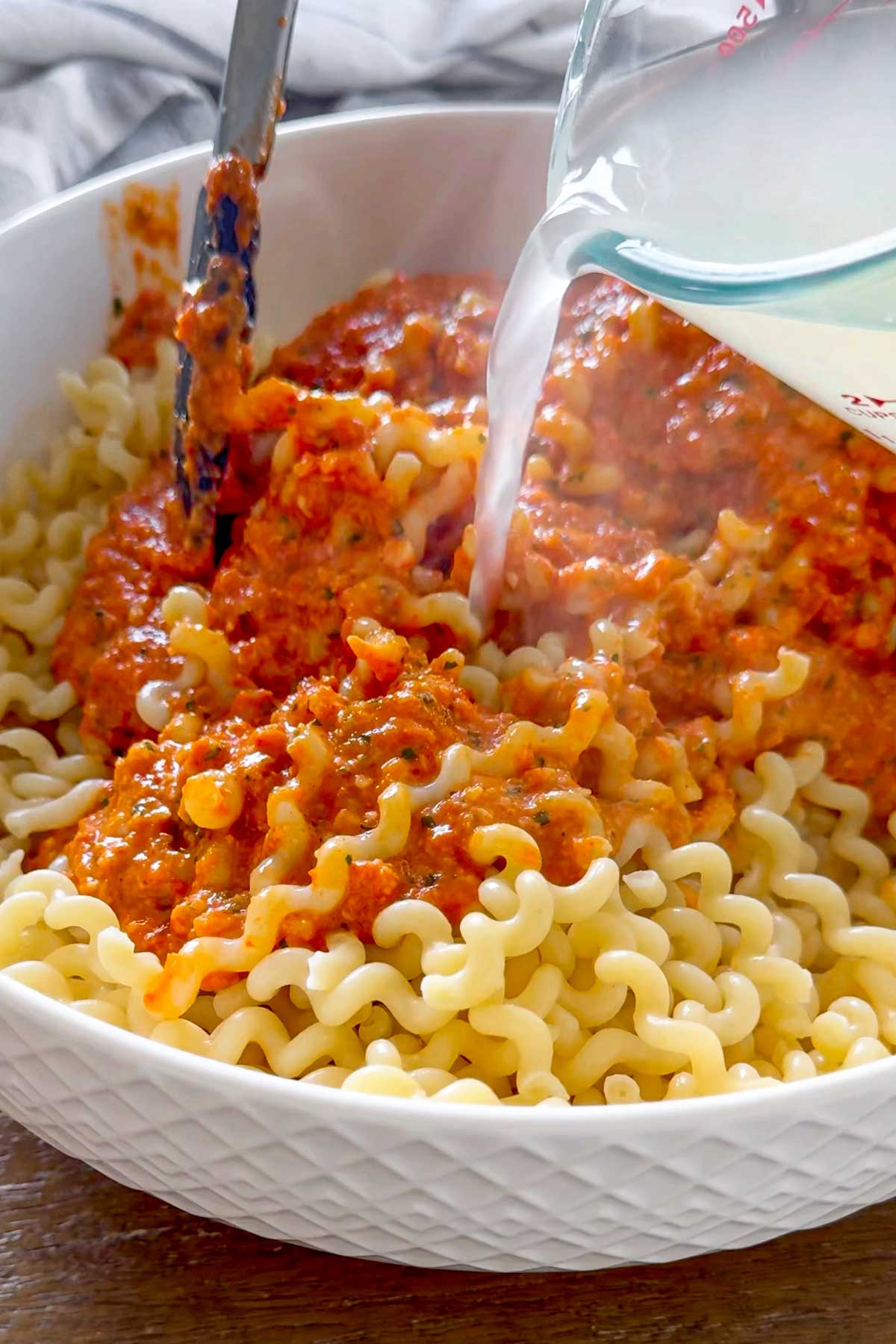 tossing cooked pasta with the sauce and pasta water