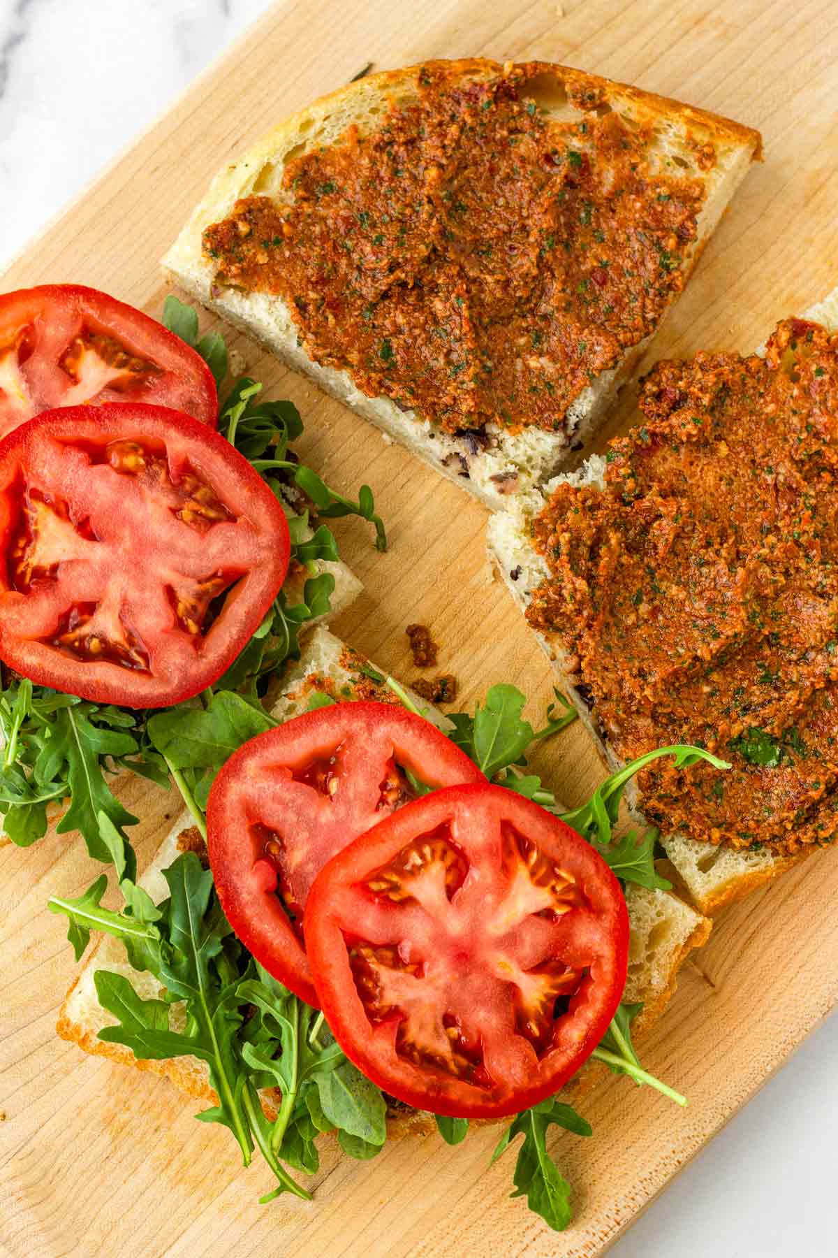 assembling sandwich with pesto, tomatoes, and arugula