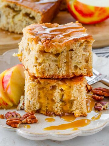two squares of fresh apple cake with caramel drizzle stacked on plate