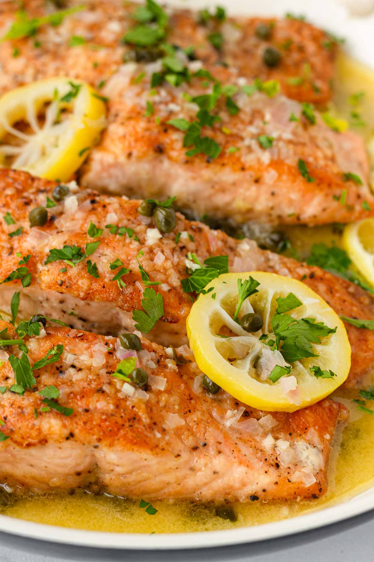 close up of salmon piccata with lemon garnish in a skillet