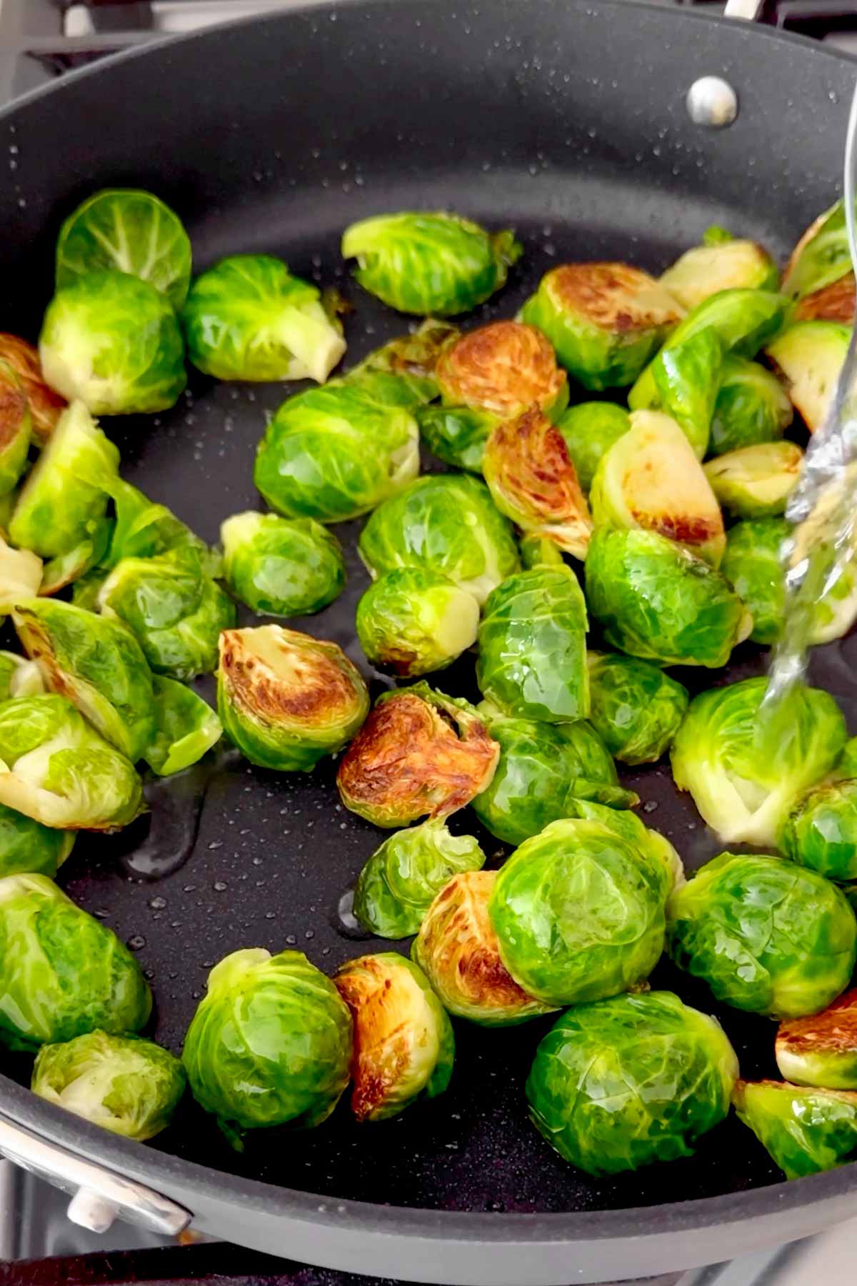 adding water to steam the sprouts in the pan