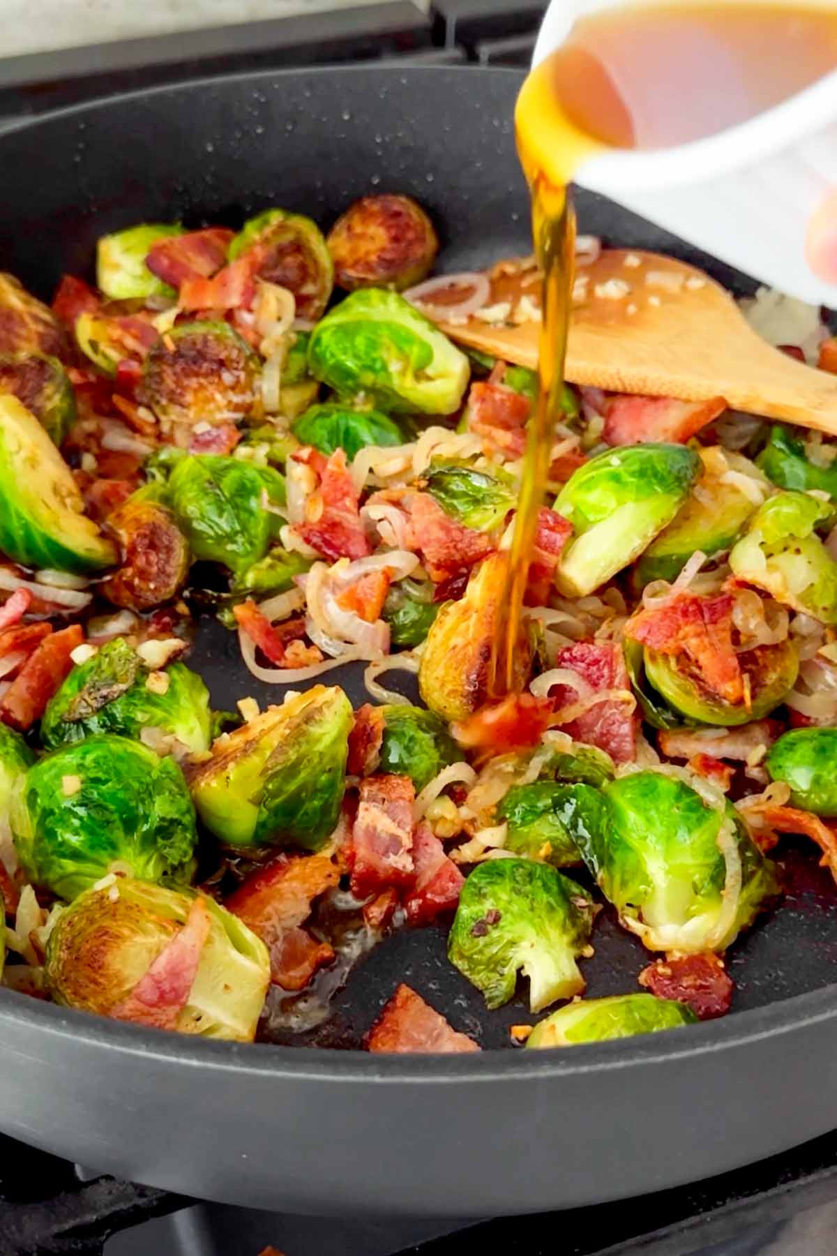 adding maple syrup to brussels sprouts with bacon in skillet