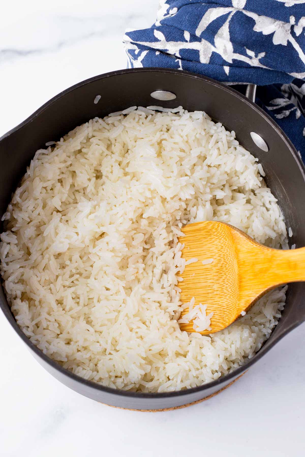 fluffing cooked coconut jasmine rice with a wooden spoon