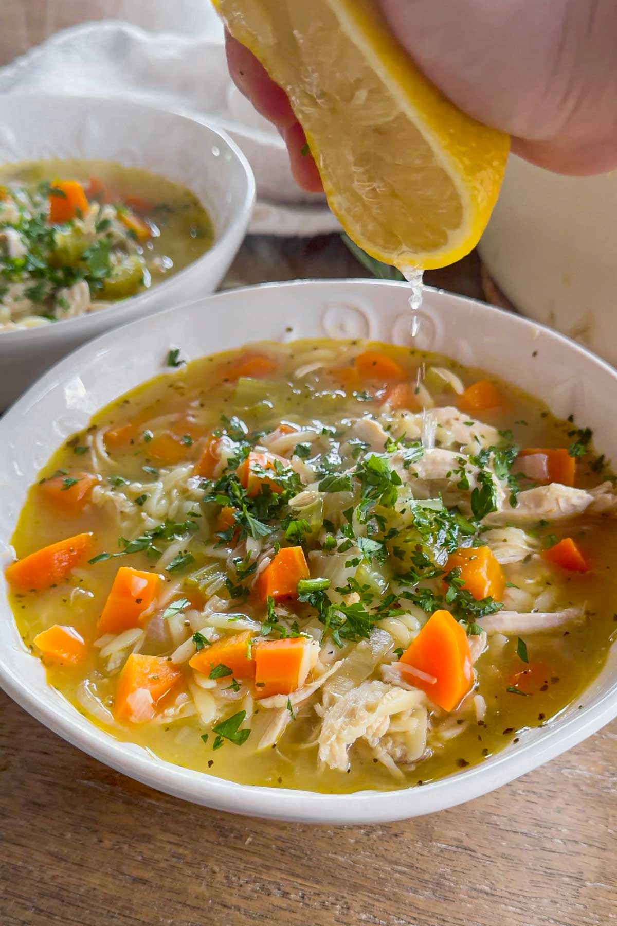 squeezing lemon into the turkey orzo soup in a bowl