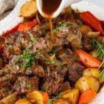 pouring gravy over slow cooked pot roast on platter