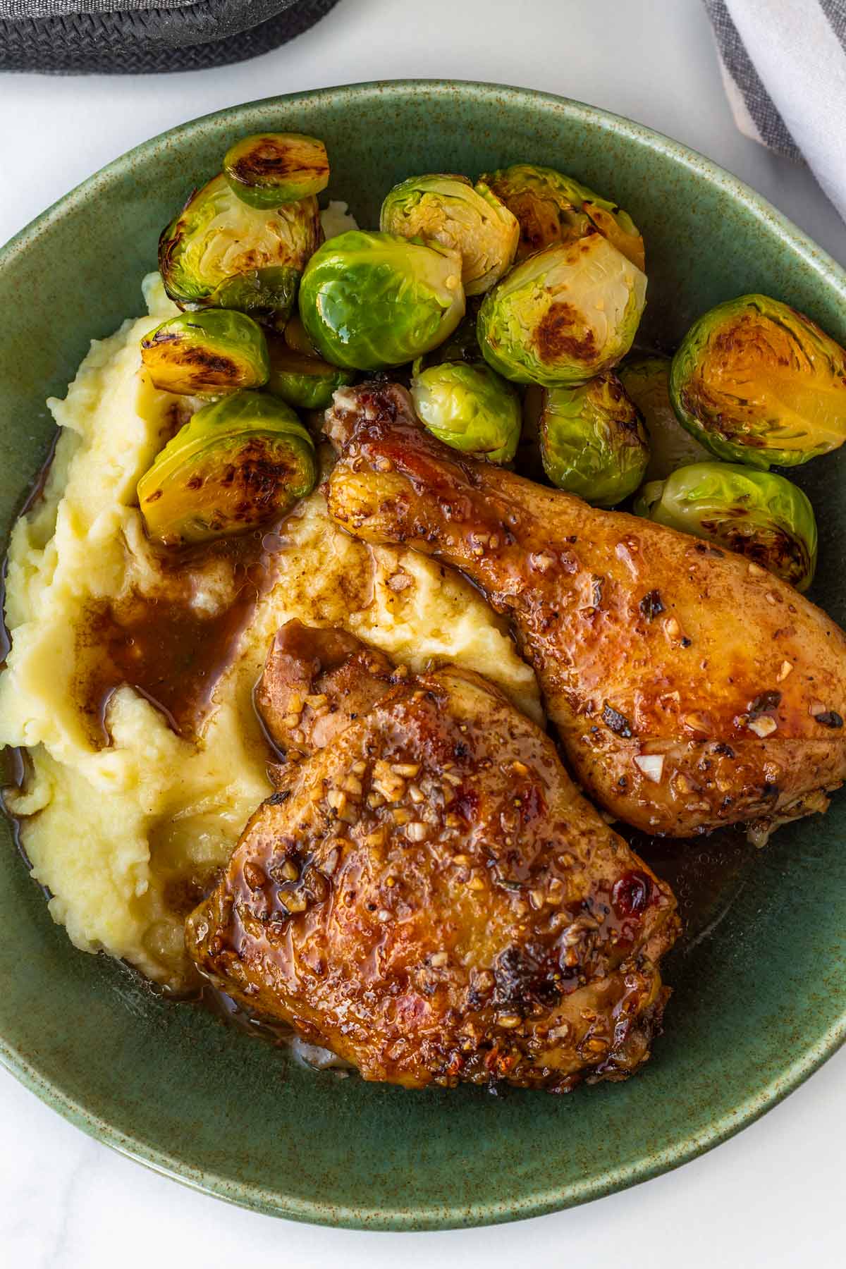 two pieces of balsamic chicken served on a bowl with mashed potatoes and brussels sprouts