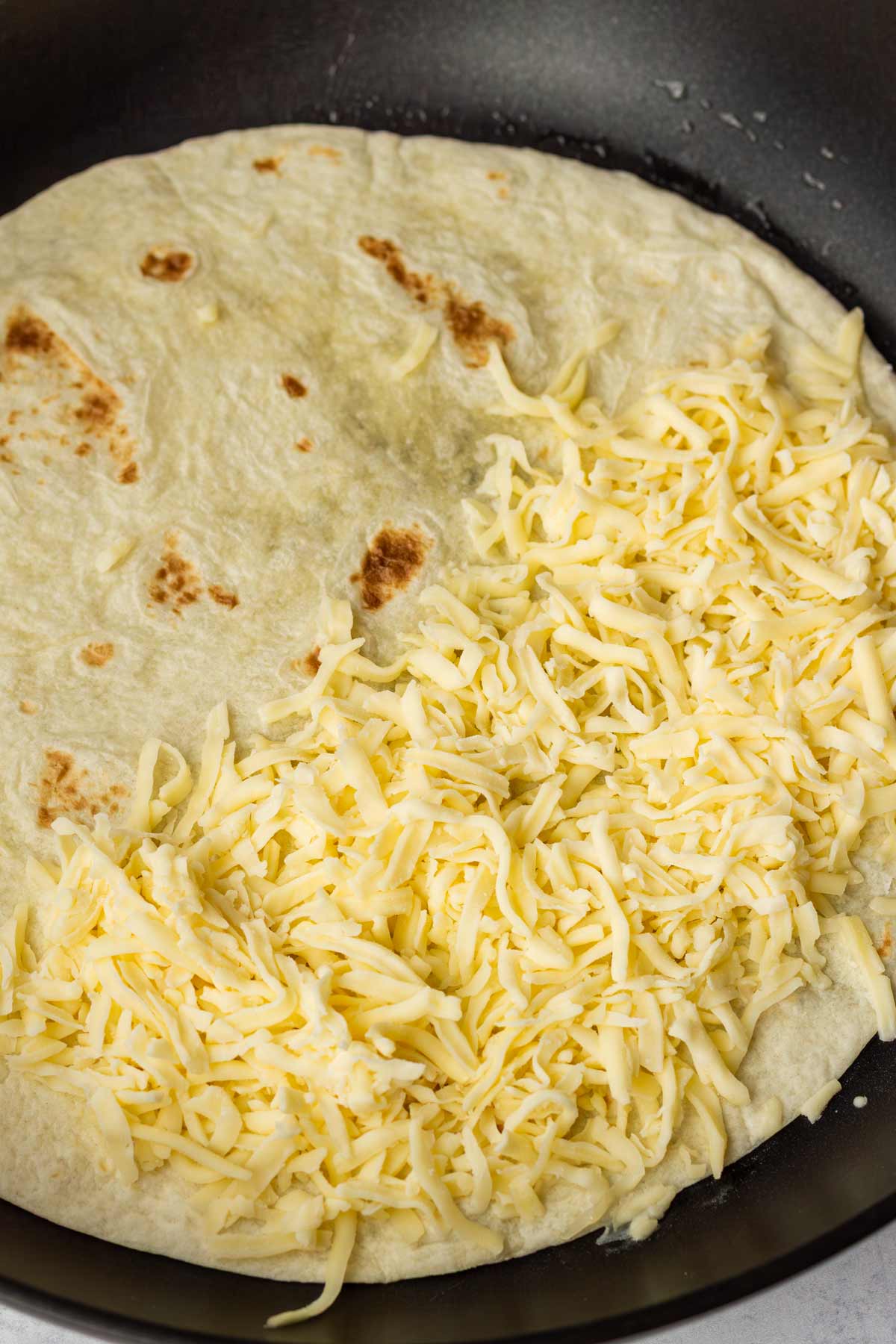 shredded cheese on one half of a flour tortilla in pan