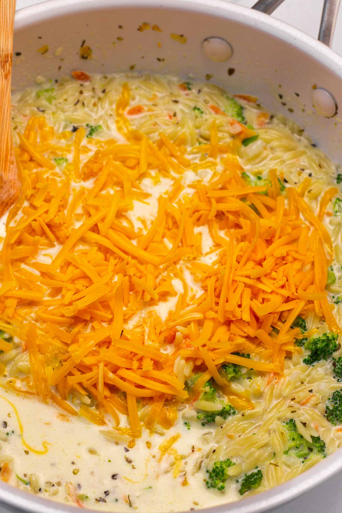 adding shredded cheddar cheese to the broccoli orzo