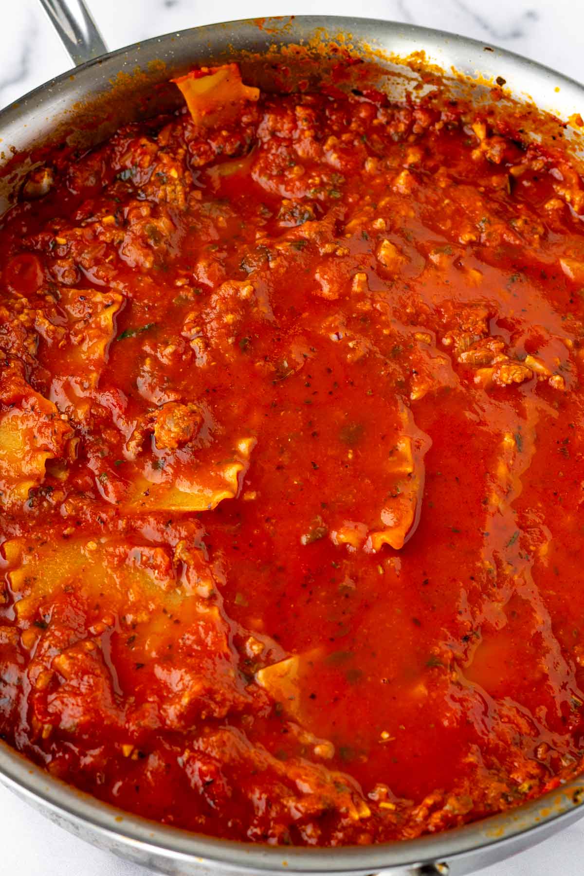 simmering lasagna noodles in the meat sauce in skillet