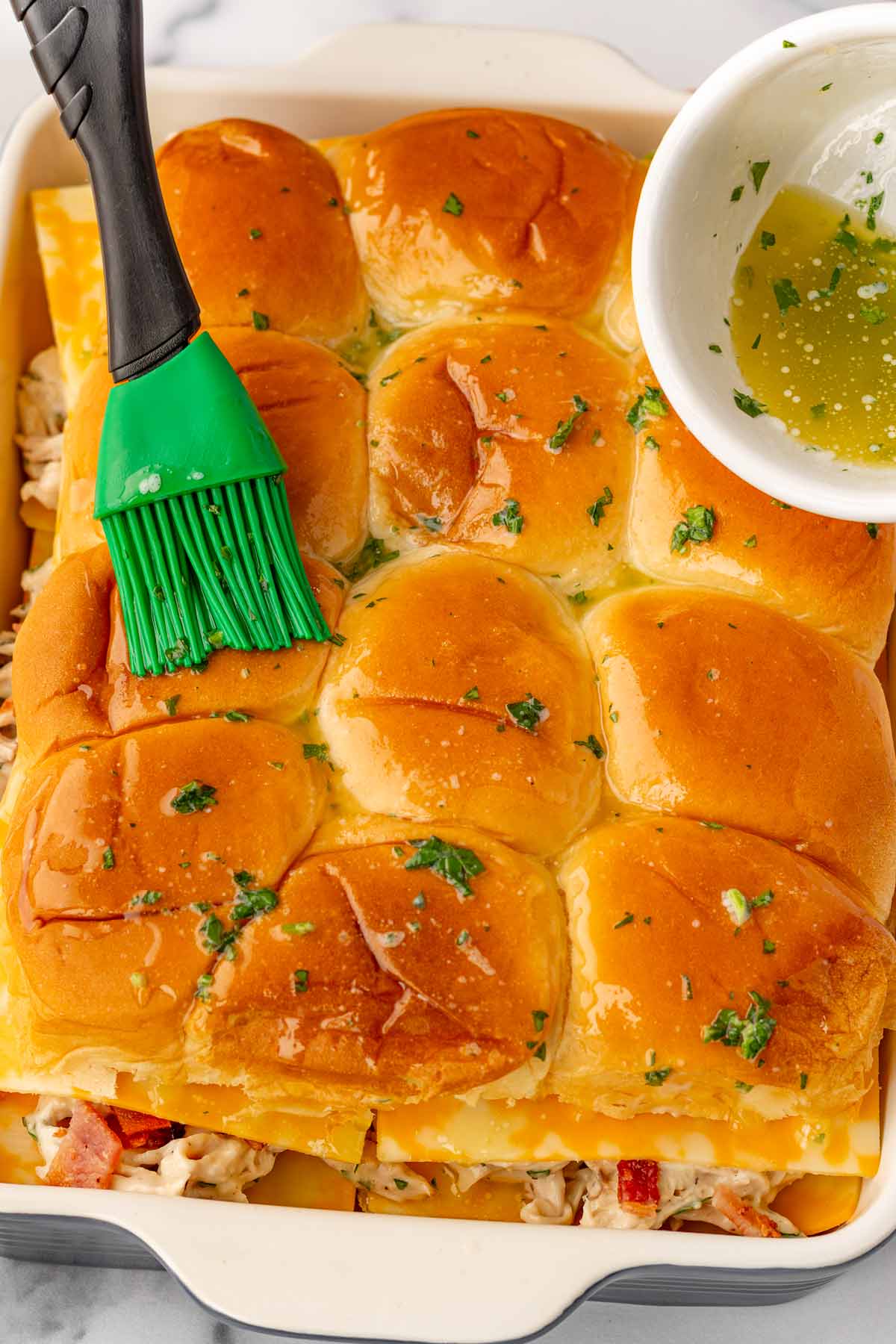 brushing assembled top slider buns with melted garlic butter