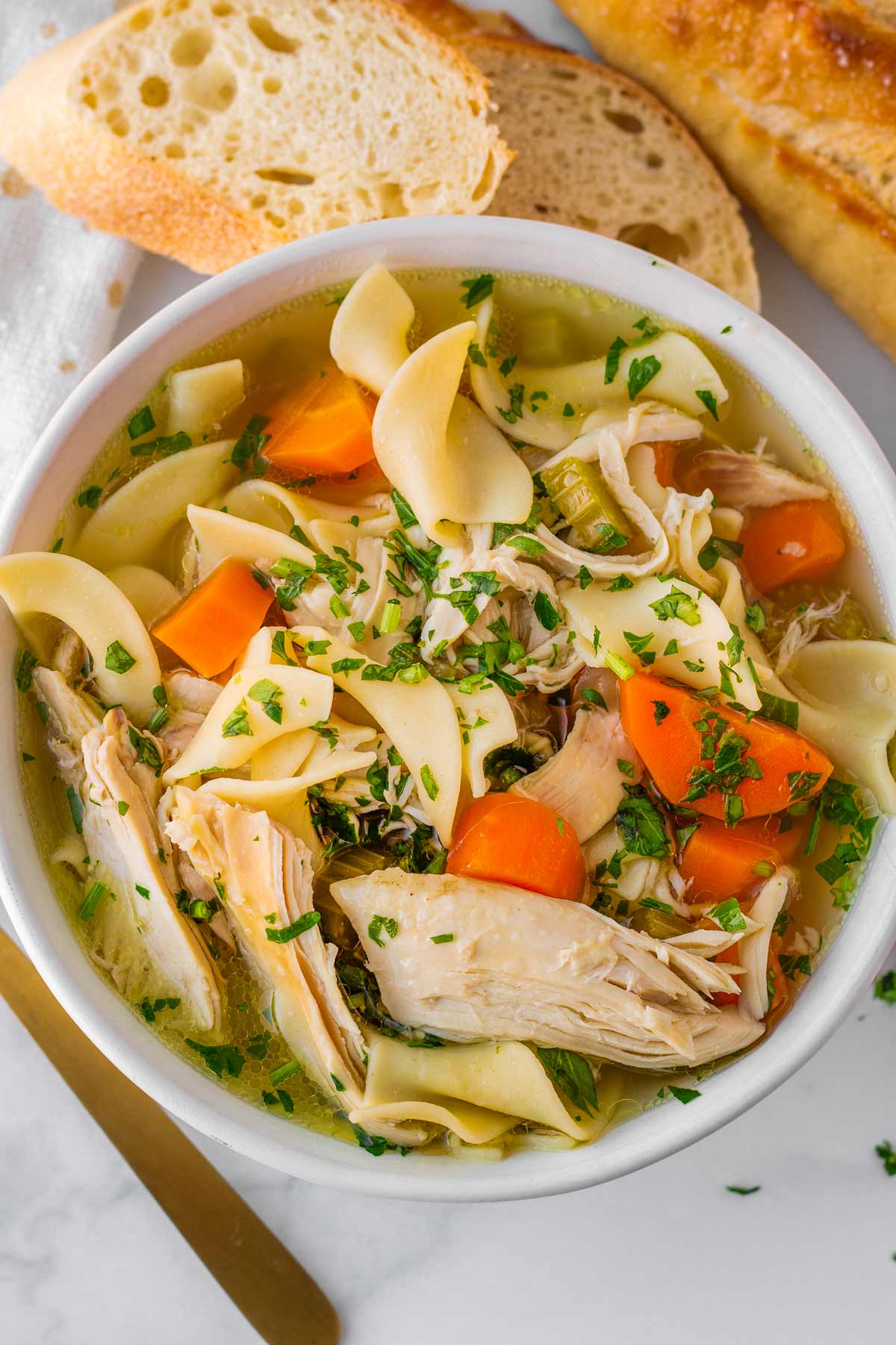 bowl of crock pot chicken noodle soup in a ceramic bowl with bread