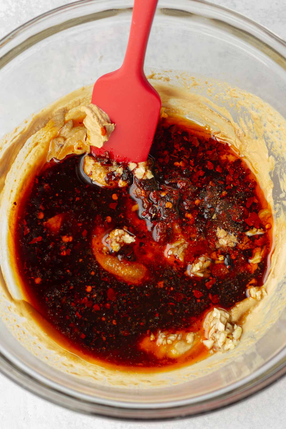 adding spices to the creamy sesame sauce in bowl