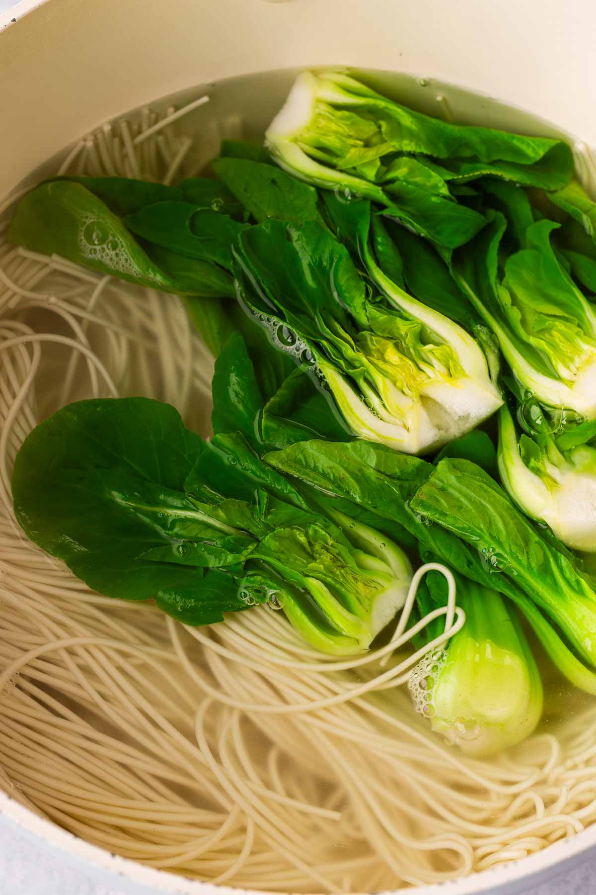 simmering wheat noodles and boy choy in a pot with water