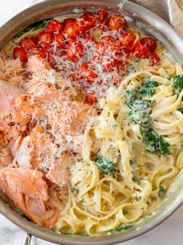 salmon pasta with tomatoes and spinach tossed in creamy garlic parmesan sauce