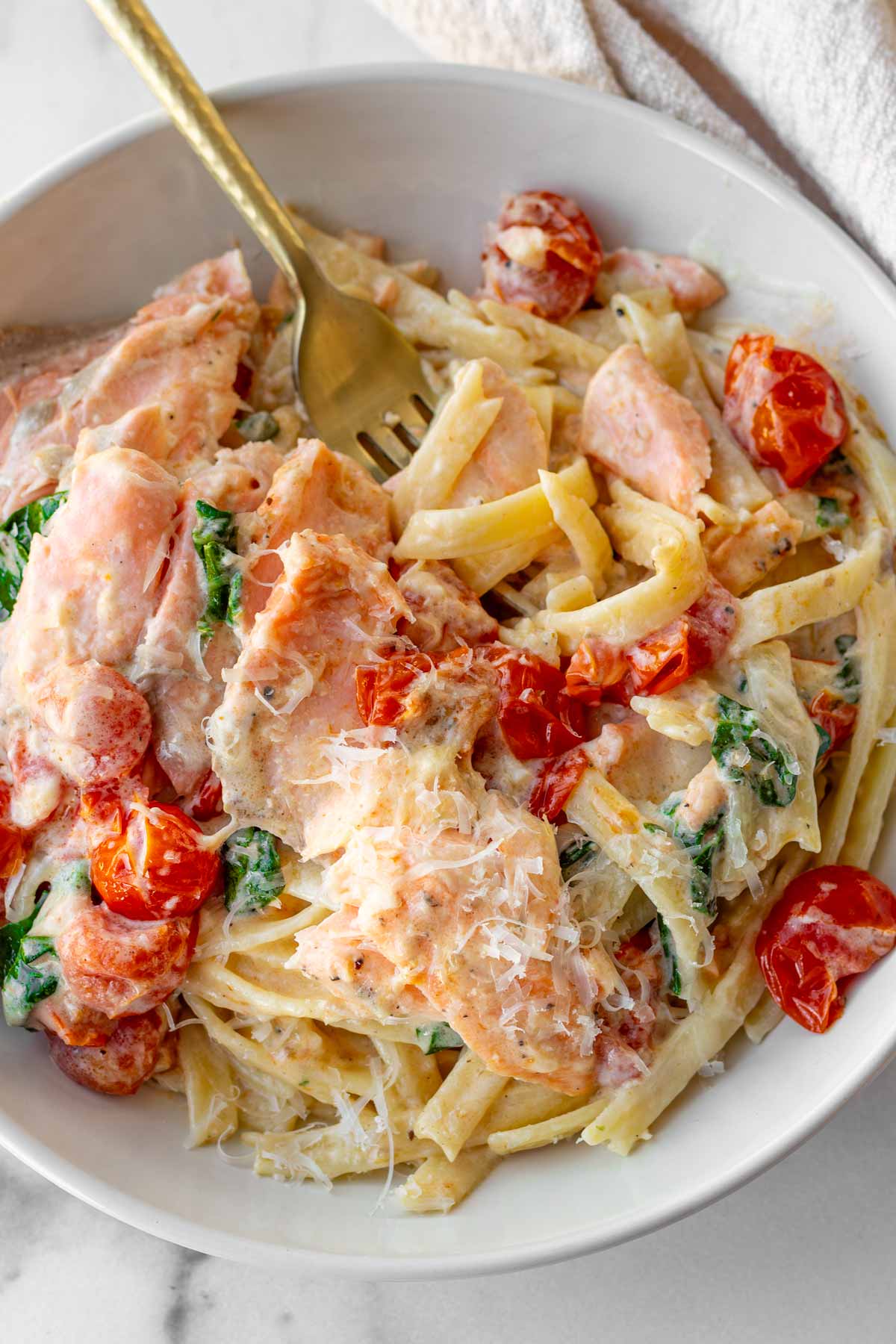 bowl with creamy sauce coating the fettuccine, salmon, and tomatoes