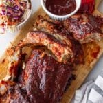 cooked baby back ribs in oven​ sliced with a side of bbq sauce and creamy coleslaw