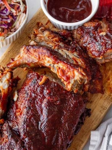 cooked baby back ribs in oven​ sliced with a side of bbq sauce and creamy coleslaw
