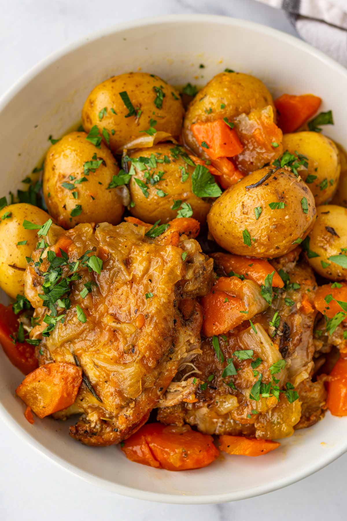 bowl of tender slow cooked chicken thighs served with potatoes and carrots