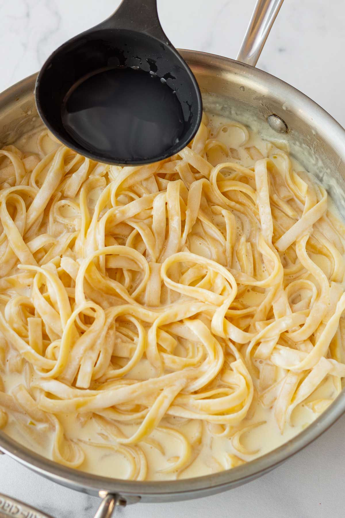 adding starchy pasta water to the fettuccine that is coated with the creamy sauce