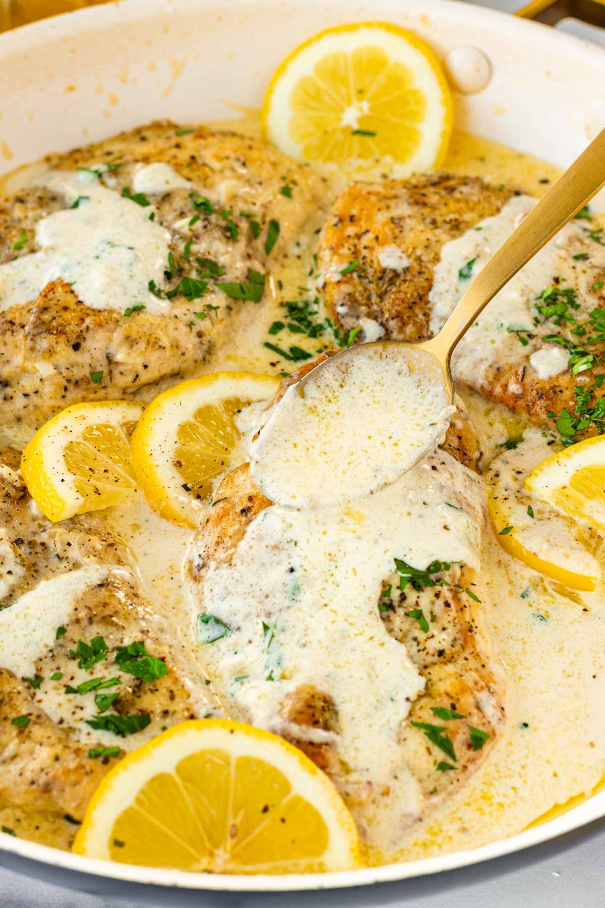 spooning creamy lemon sauce over the chicken