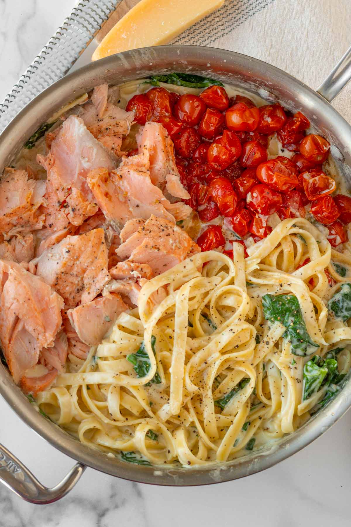 stainless steel skillet with fettuccine tossed in creamy sauce plus salmon and tomatoes on the side