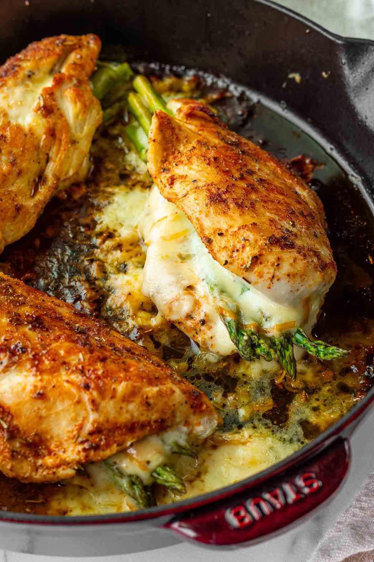seared asparagus stuffed chicken breast with melty gouda in a cast iron skillet
