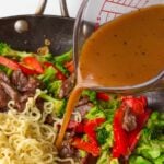 adding stir fry sauce to noodles in pan