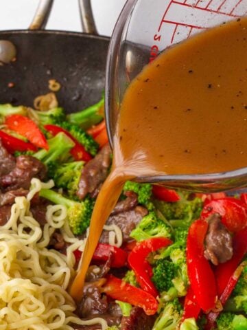adding stir fry sauce to noodles in pan