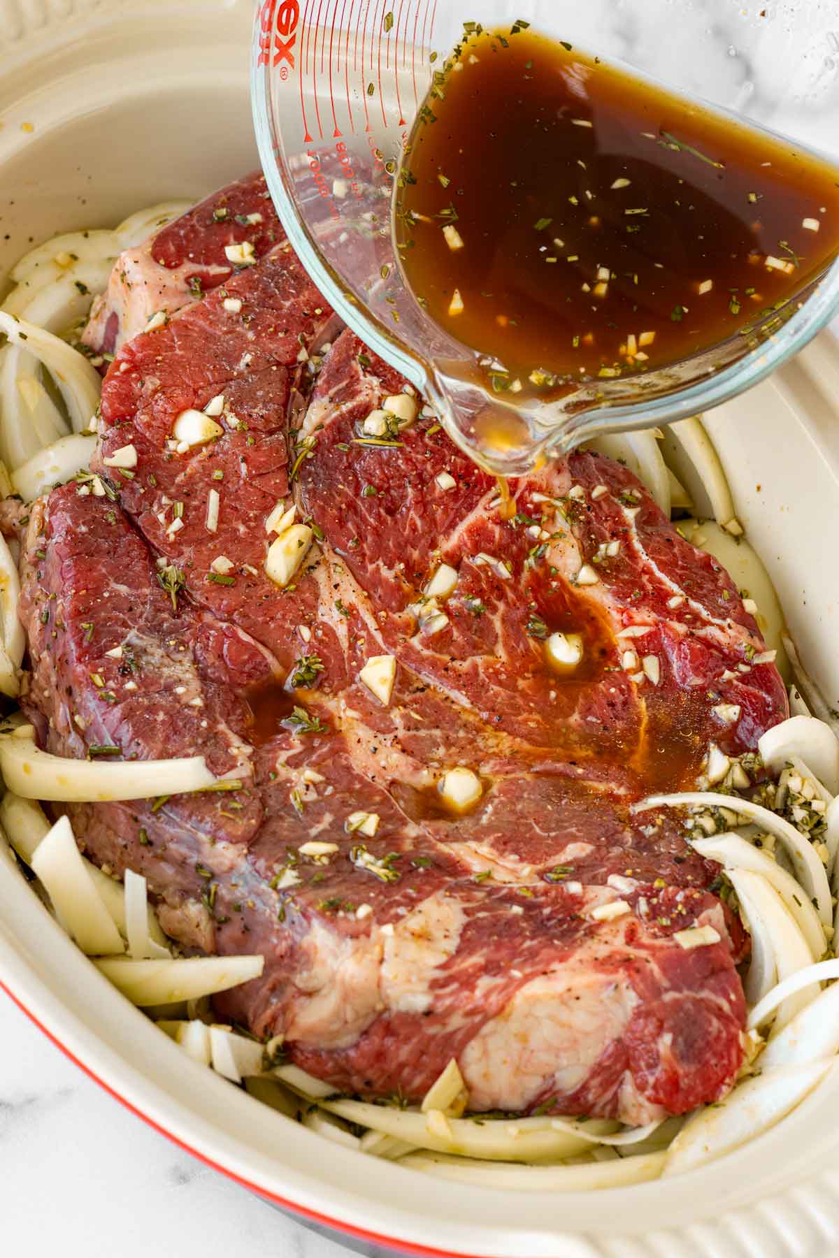 pouring braising liquid over the beef in a pan
