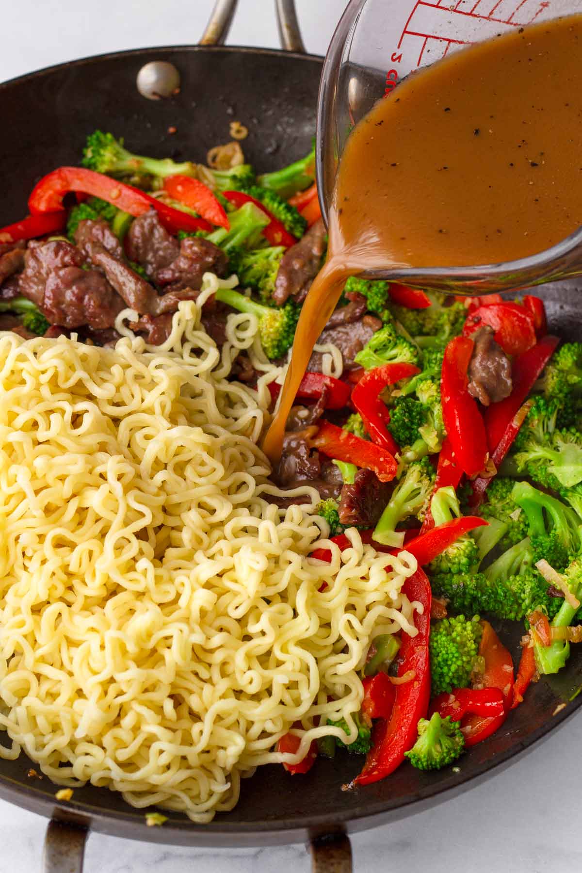adding sauce into a pan with noodles, veggies, and beef