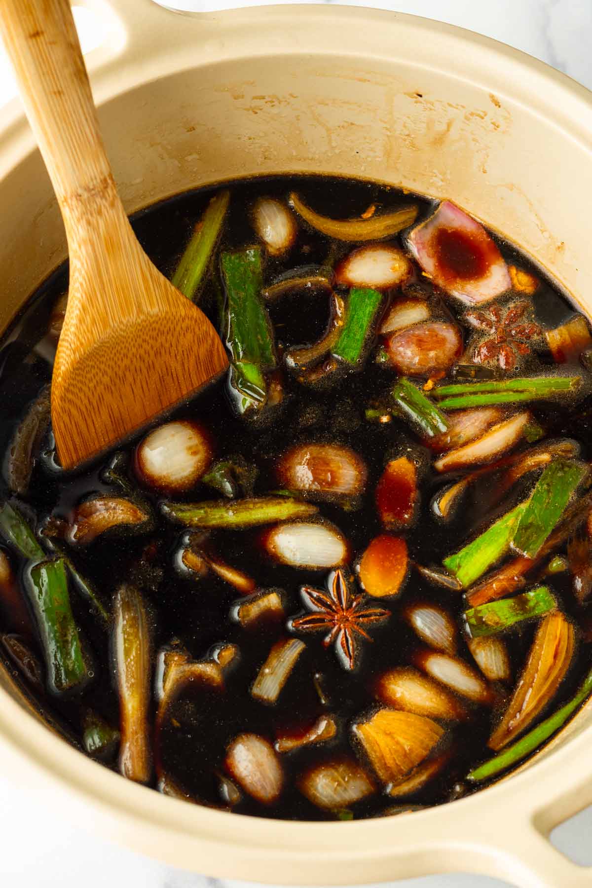 adding soy sauce and water to the aromatics in the pot