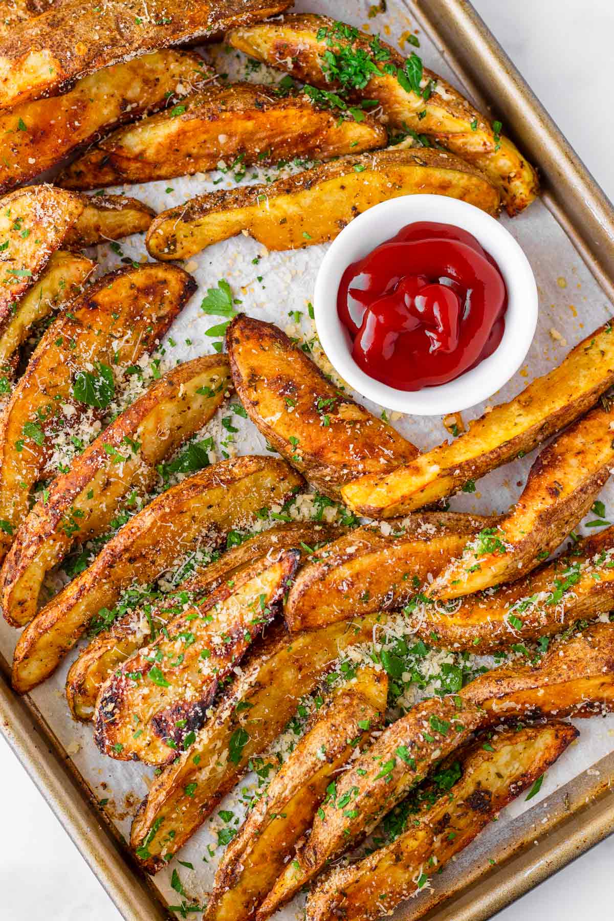 baked roasted potato wedges on sheet pan with a little bowl of ketchup