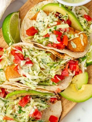 baja fish tacos with slaw, avocado crema, tomatoes, limes