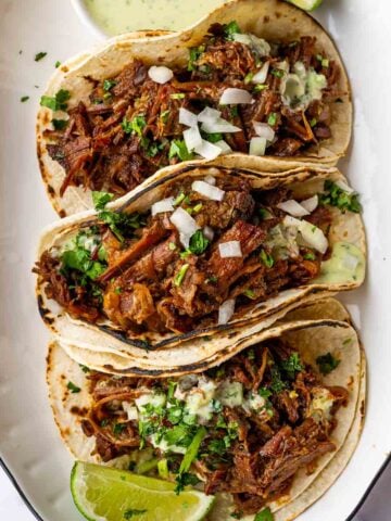 three generously filled shredded beef tacos on oval platter