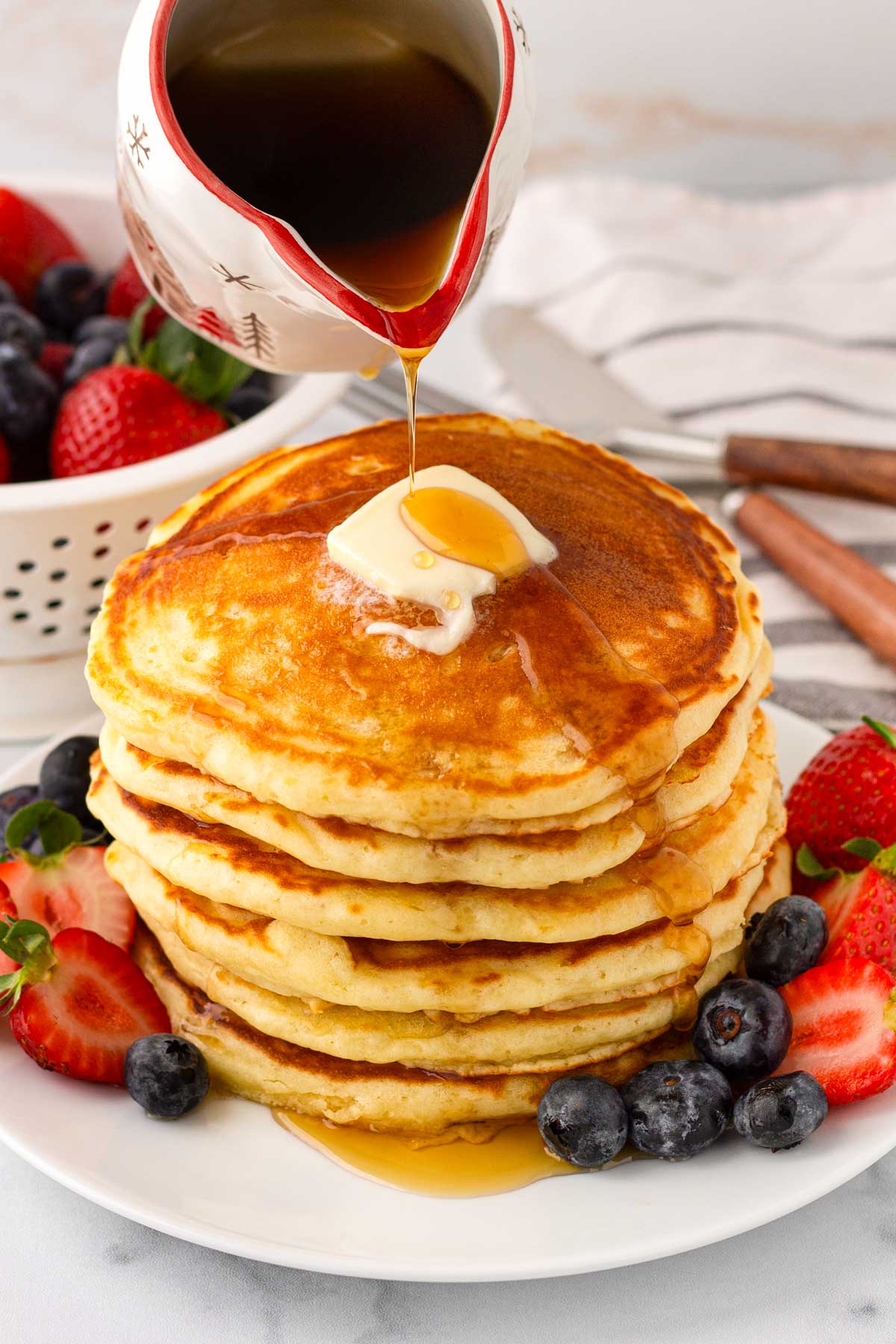 stacked fluffy buttermilk pancakes with berries and maple syrup and butter on top