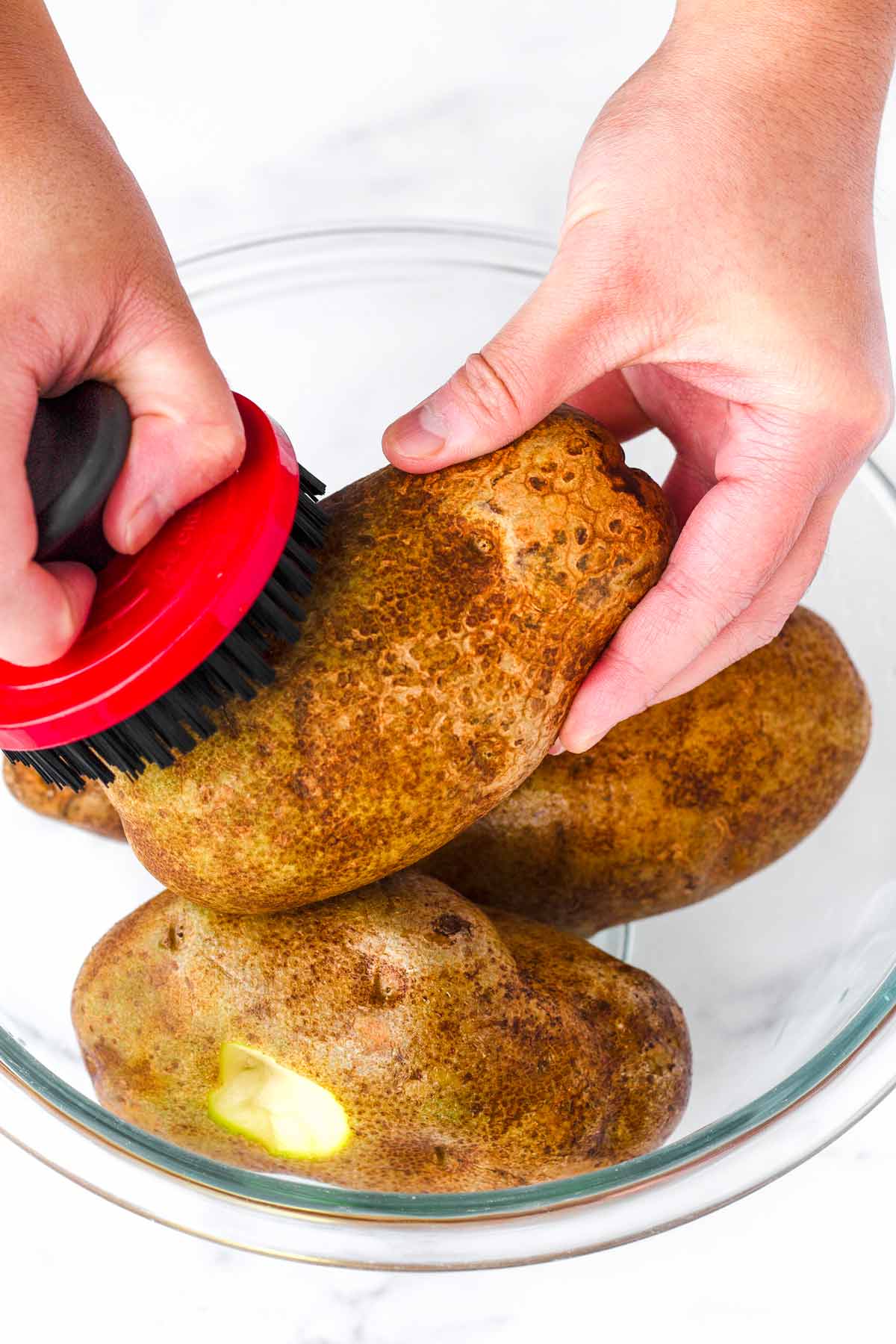 scrubbing russet potatoes clean using a brush