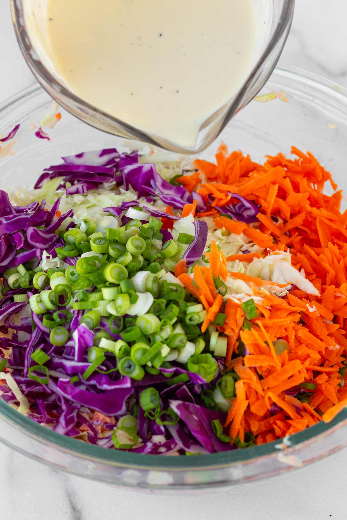 adding the dressing into a bowl with the coleslaw ingredients