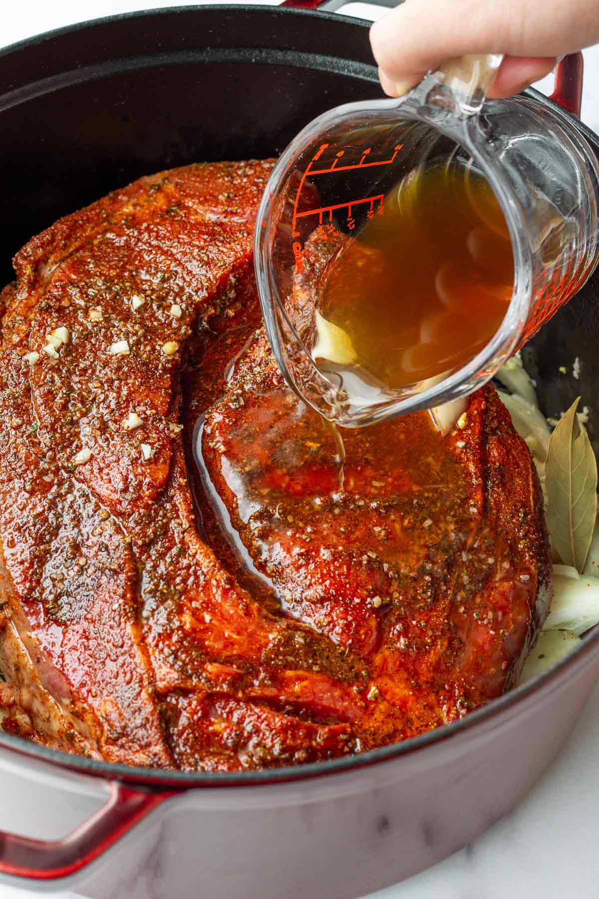 adding beef broth into the dutch oven with seasoned chuck roast