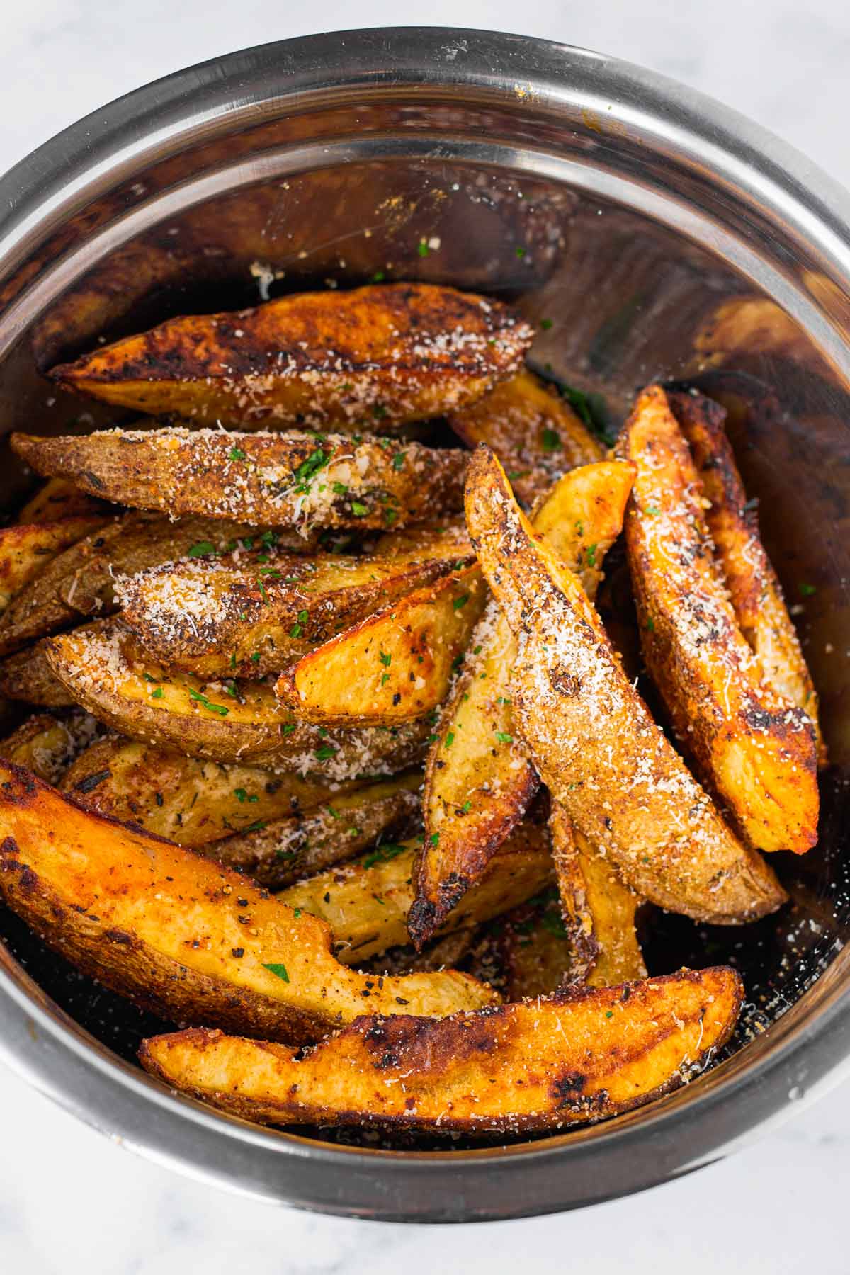 tossing roasted potatoes with parmesan and parsley in a metal bowl