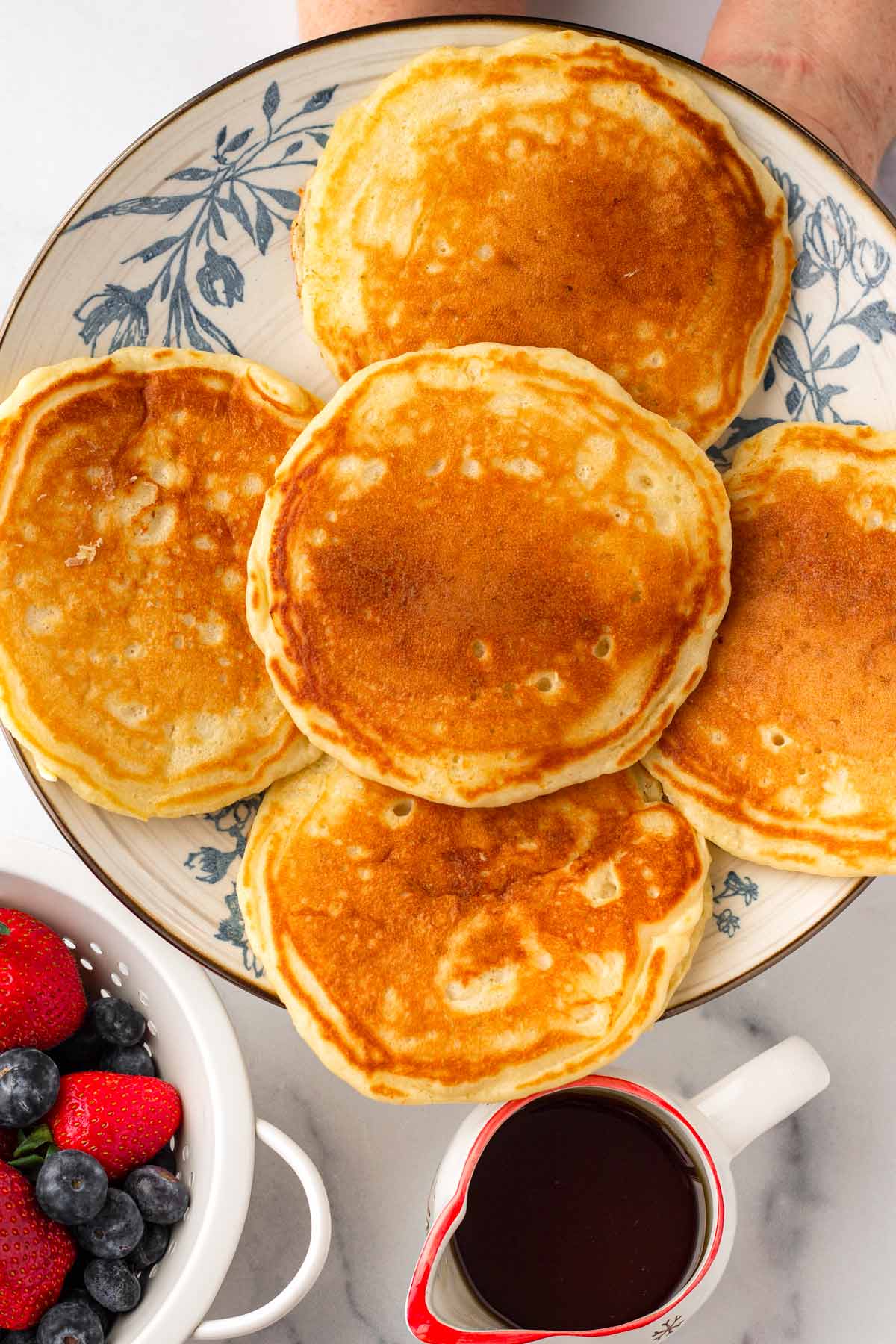 holding a platter of buttermilk pancakes with a side of fruits and syrup